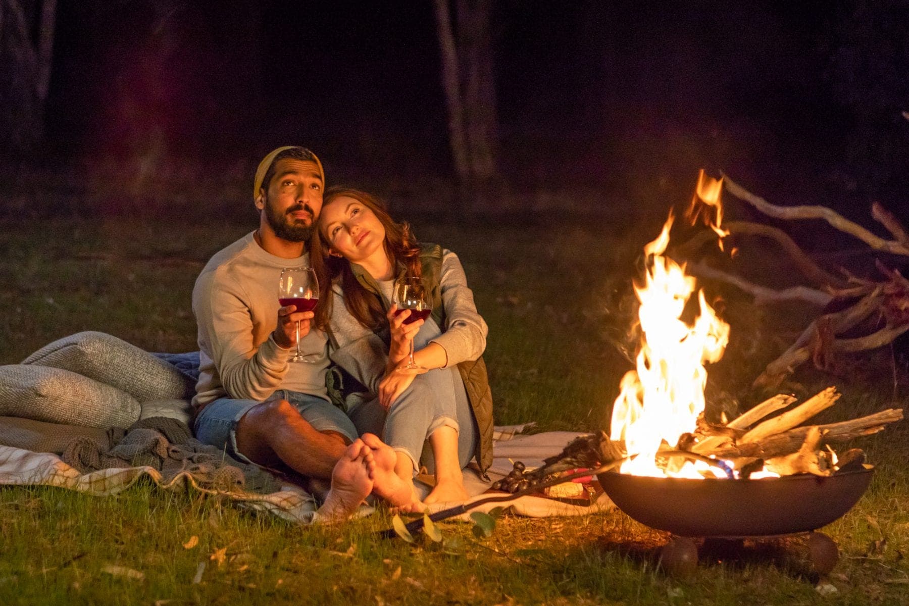 A couple wrapped in a blanket beside the fire pit after dark