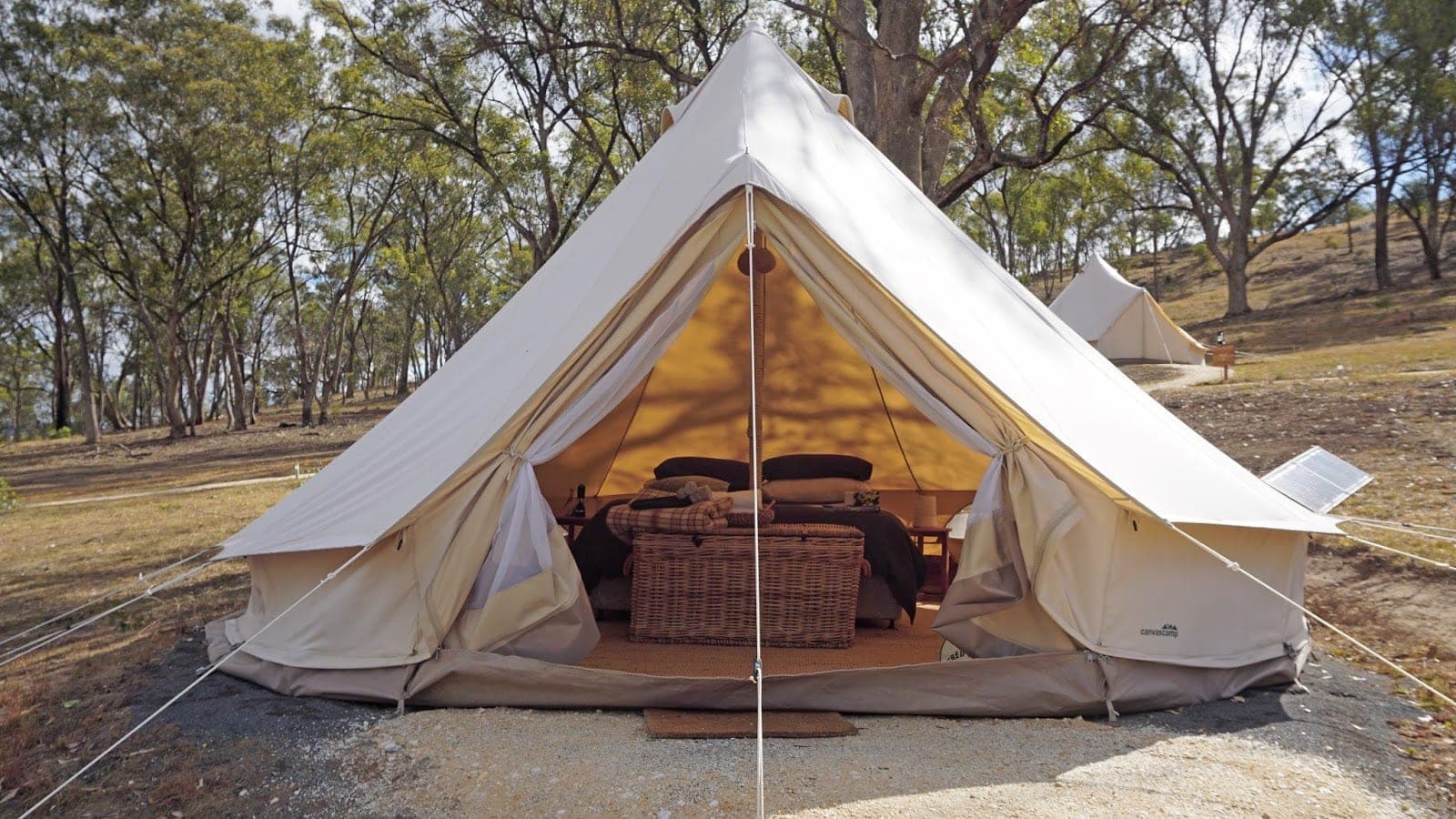 A bell tent with its canvas doors tied open, on a gravel pad under the gums