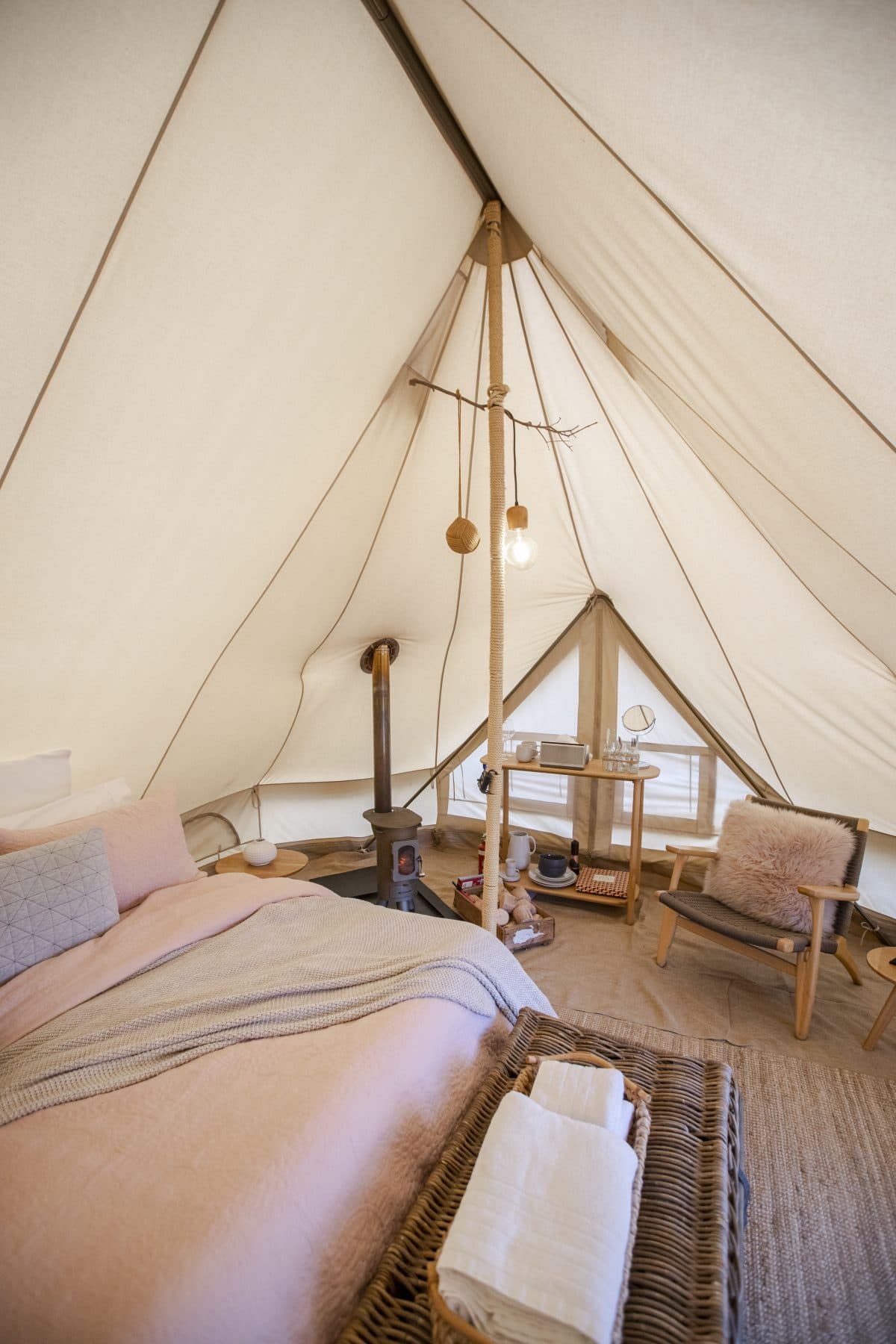 A chair beside the wood heater inside a bell tent, the doors open to the bush
