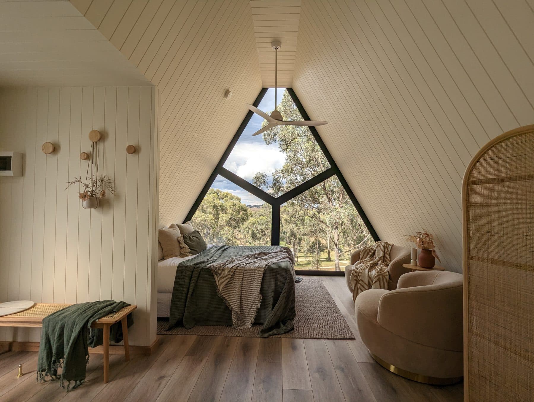 Inside the cabin: the bed, the glazed gable and a rattan chair