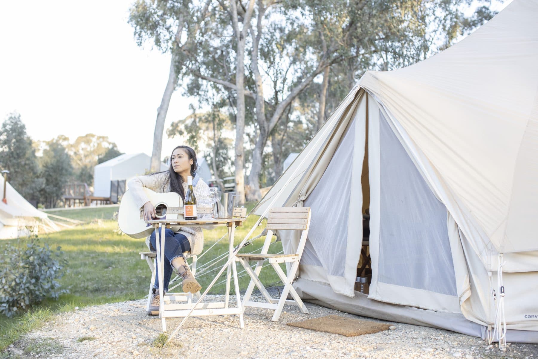 A guest playing guitar in a chair outside her bell tent
