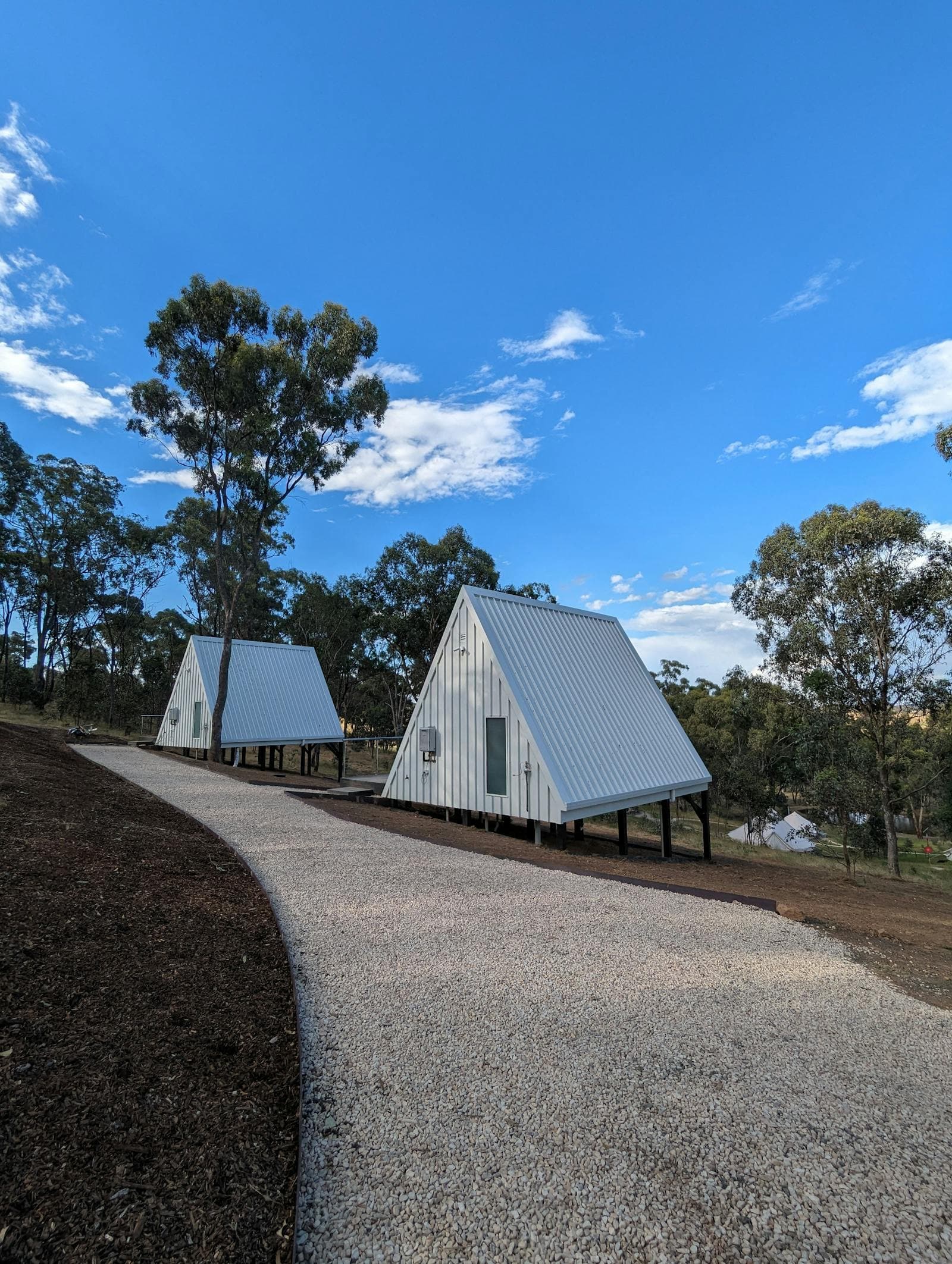 Two A-Frame cabins beside the gravel path under a blue sky
