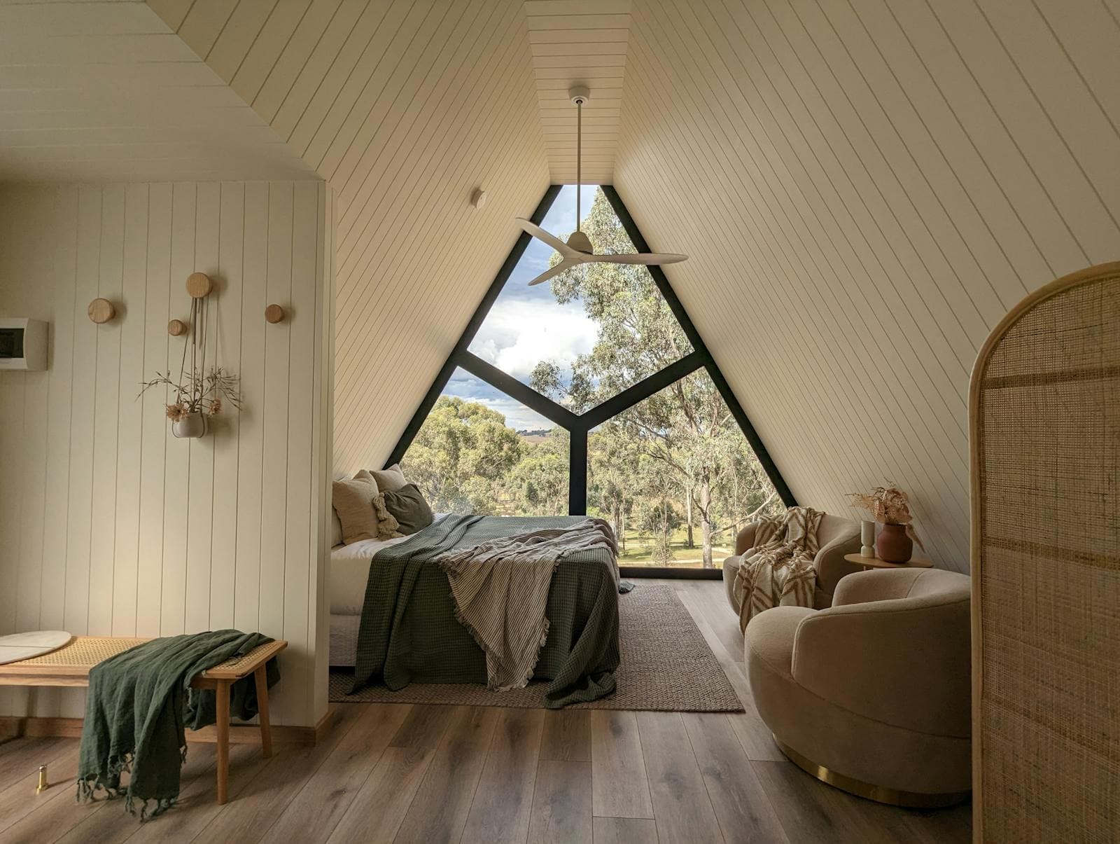 Inside the cabin: the bed, the glazed gable and a rattan chair