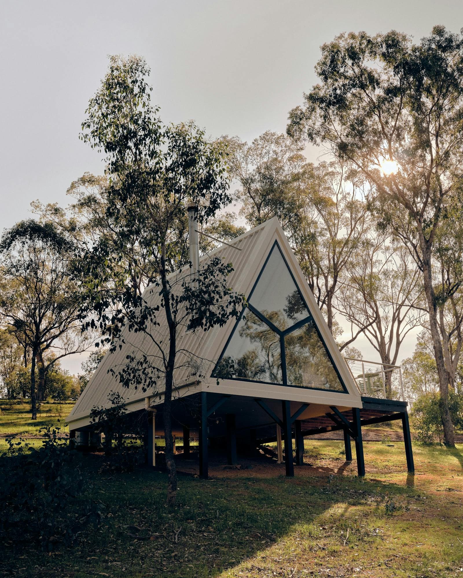 An A-Frame cabin seen from the path, gum trees behind it