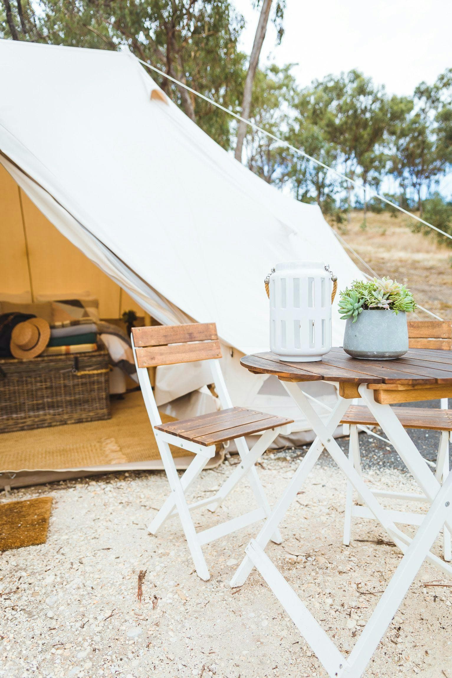 A table and chairs set outside a Luxe tent, with a lantern and a pot plant