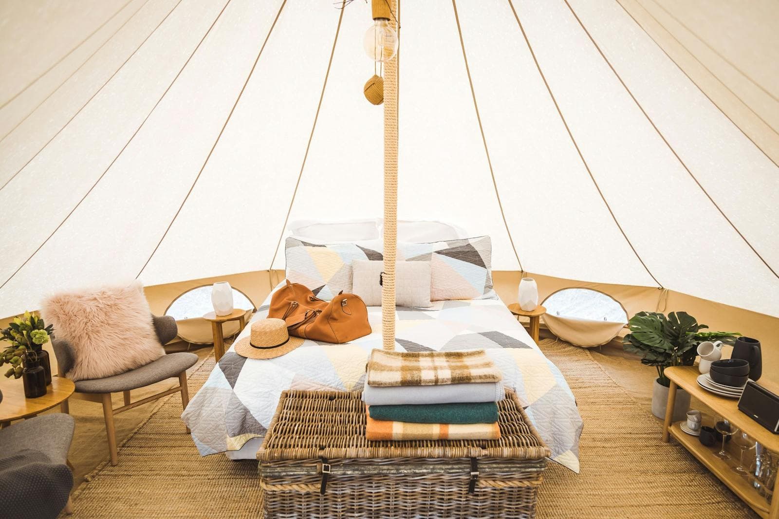 The queen bed, lounge and woven basket inside a bell tent, lit through the canvas
