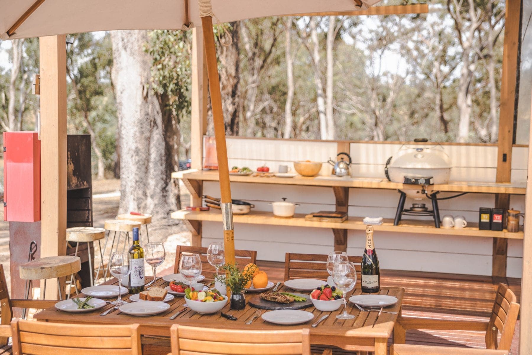 The camp kitchen — Weber barbecue, gas burner and a laid table under the trees