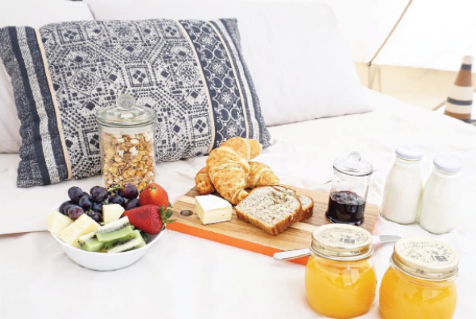 Breakfast laid out on the bed: croissants, fruit, cereal jars, milk and juice
