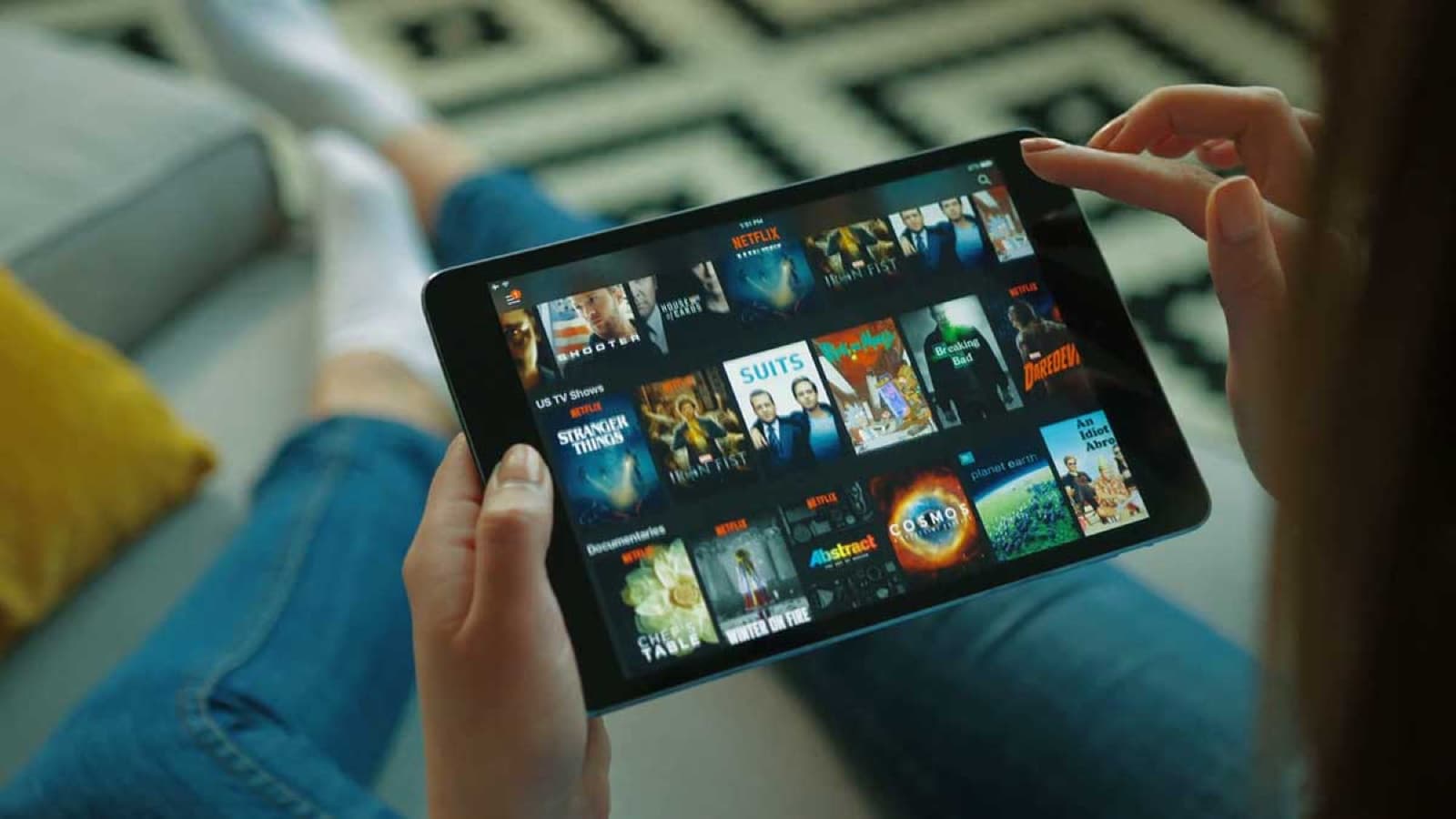 Hands holding a tablet showing a grid of shows to choose from
