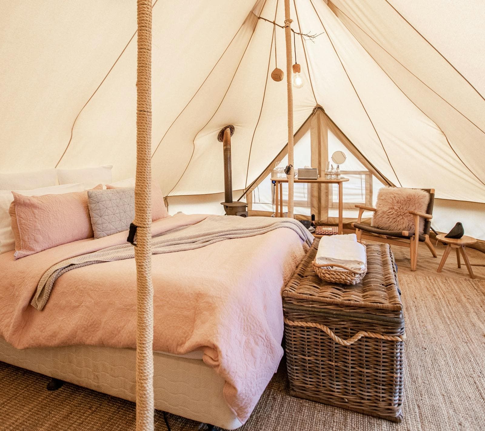Inside a Luxe bell tent: the queen bed in blush linen, a timber bedside and a woven basket