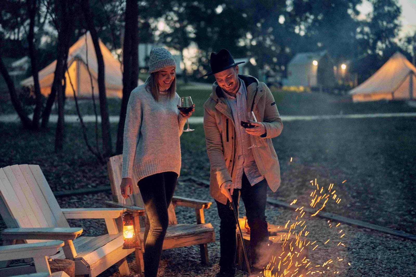Two guests with a glass of wine beside the fire pit after dark